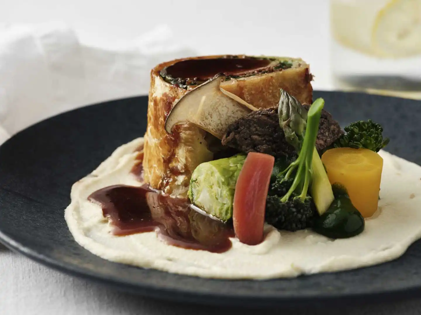 Gourmet dish with vegetables and sauce on a black plate.