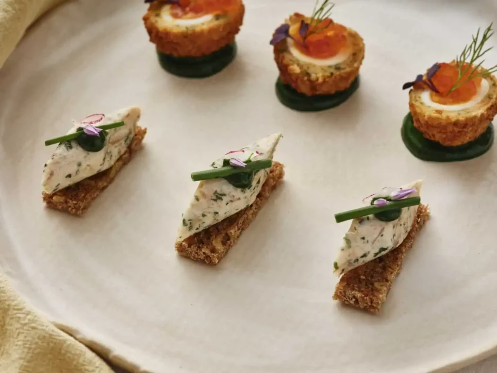 Elegant appetizers on a white plate, featuring savory bites with herbs and garnishes.