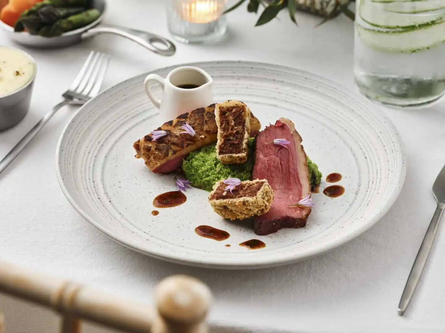 Elegant plated dish with meat, sauce, and garnish on a white table setting.